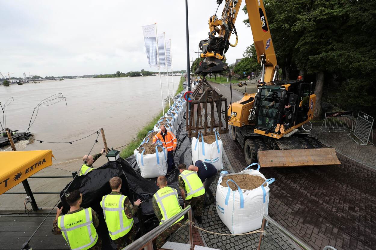 Defensiemedewerkers en een graafmachine bij een tijdelijke waterkering langs de Maas tijdens het hoogwater van juli 2021.